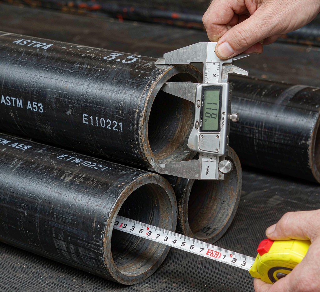 Carbon steel welded pipe being measured with ultrasonic wall thickness gauge